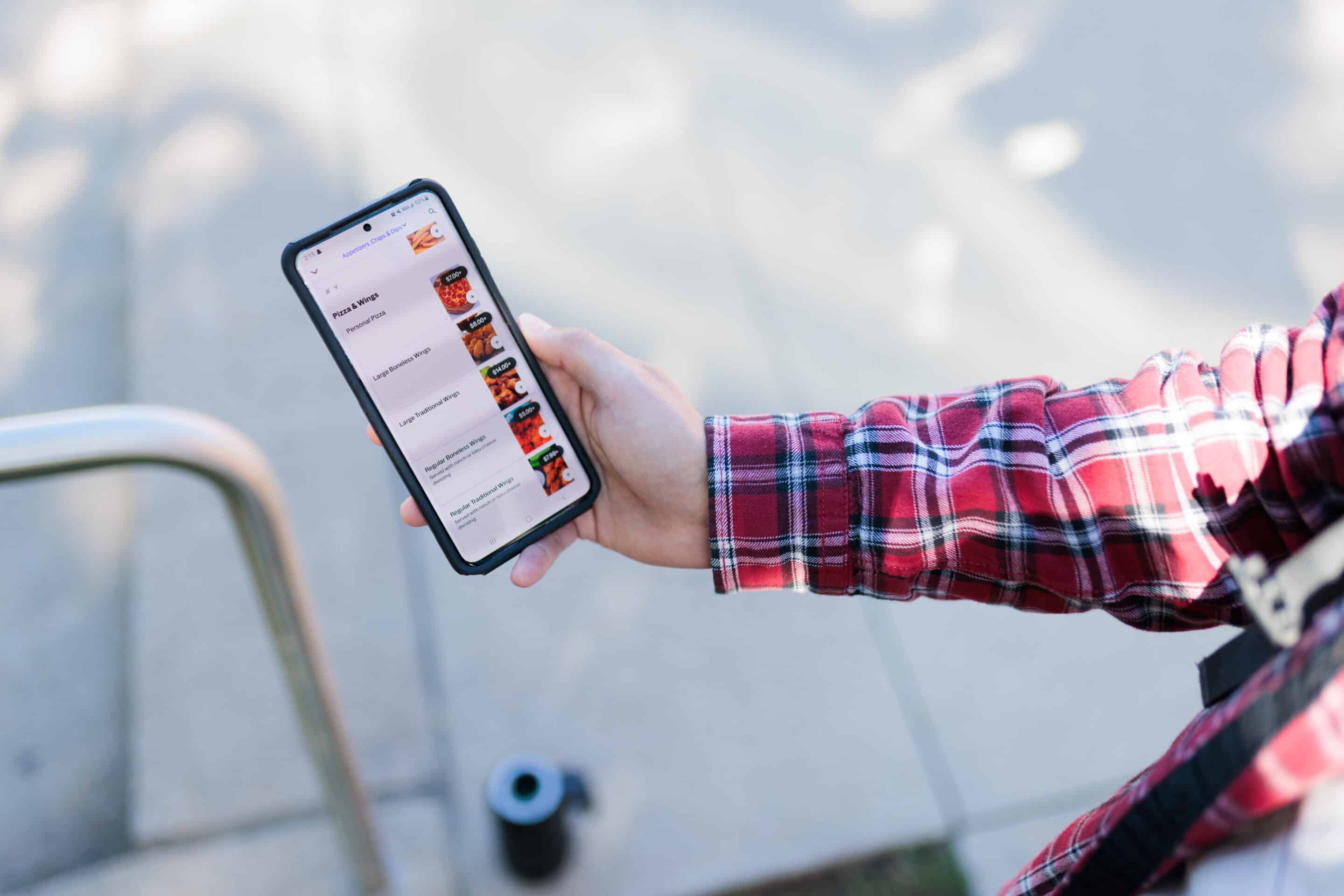 person in red flannel shirt holding a smartphone outside that ordered ahead